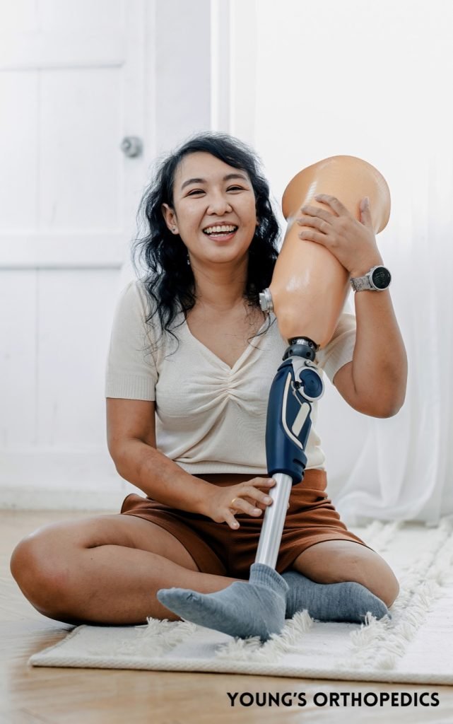 Smiling patient sitting on the floor holding a custom below-knee prosthetic leg